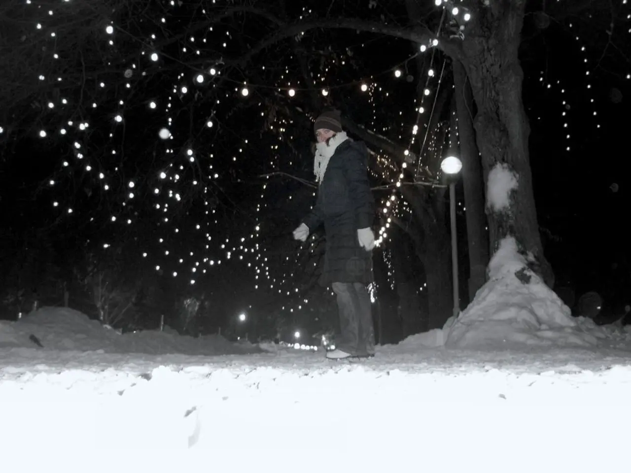 In the foreground there is snow. In the center of the picture there is a person walking. In the...