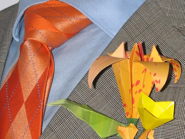 As we can see in the image there is orange color tie, grey color jacket and flower.